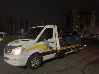 Platforma albă fotografiată din față noaptea, cu autoturism albastru transportat
