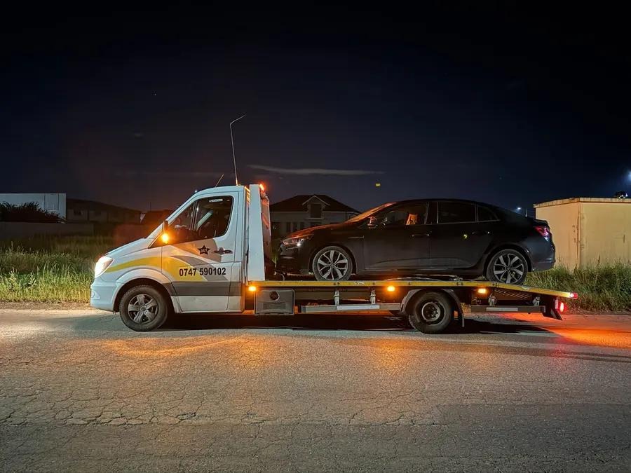 Platforma Mercedes-Benz Sprinter albă cu autoturism transportat, fotografiată noaptea