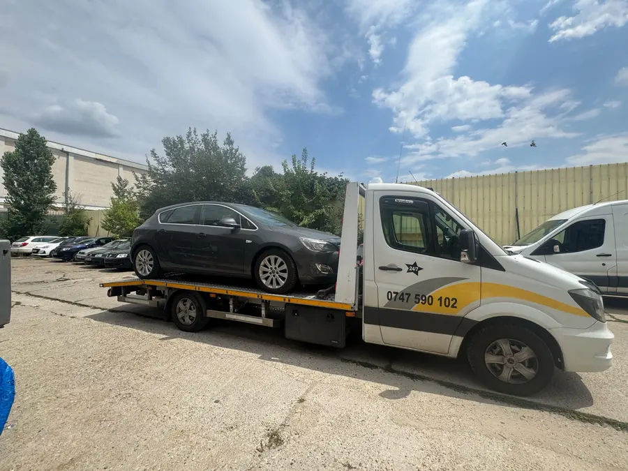 Platforma Sprinter cu un autoturism gri închis, fotografiată lateral ziua